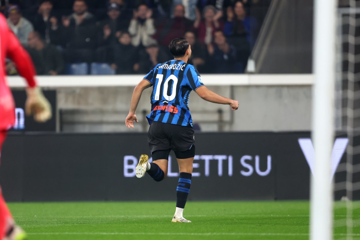 Soccer player in blue and black striped jersey with number 10 runs toward the goal on a green field, crowd visible in the stands behind.