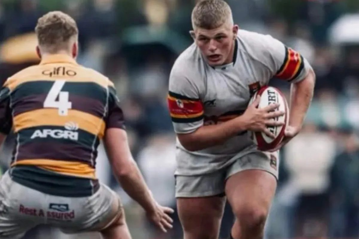 Rugby player in gray runs with the ball, facing a defender in a yellow-and-green striped jersey.
