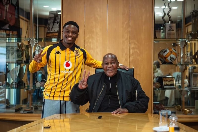Two men smile and flash peace signs in a wood-paneled office, one in a yellow striped soccer jersey standing beside a seated man at a desk. Two men smile and flash peace signs in a wood-paneled office, one in a yellow striped soccer jersey standing beside a seated man at a desk.