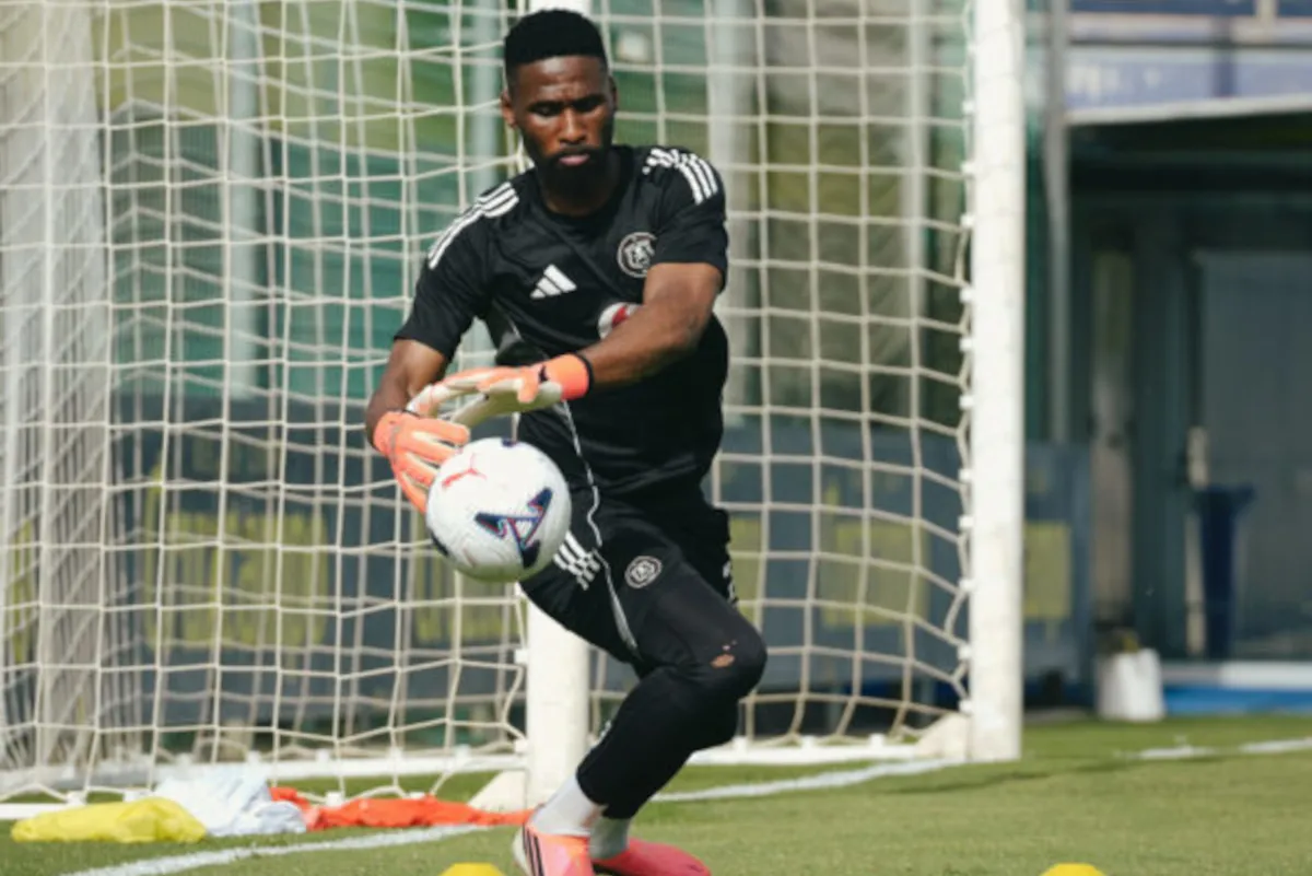 Soccer goalkeeper in black kit catching a white ball in the goal net.