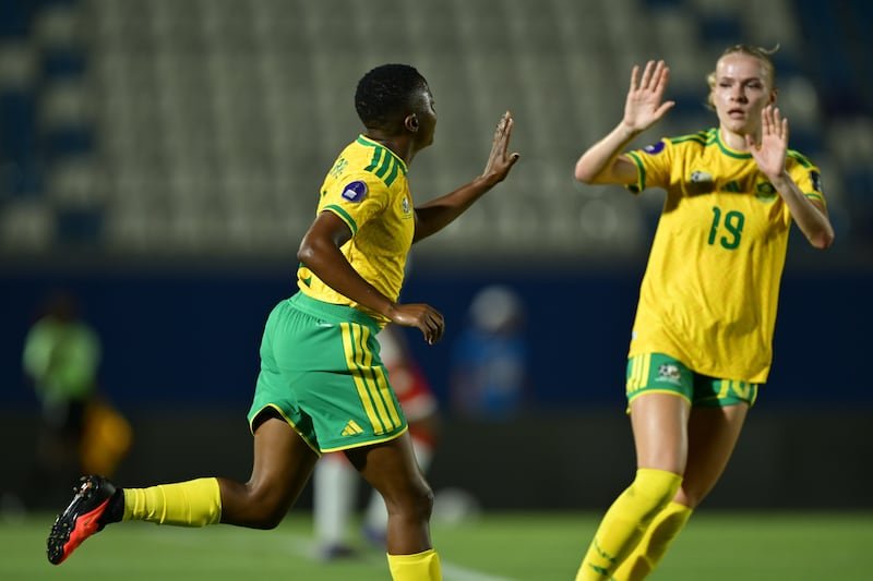 Two soccer players in yellow and green uniforms high-five on the field during a match.