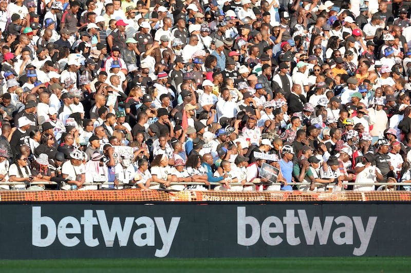 Large crowd of sports fans standing along a stadium railing behind banners that read betway.