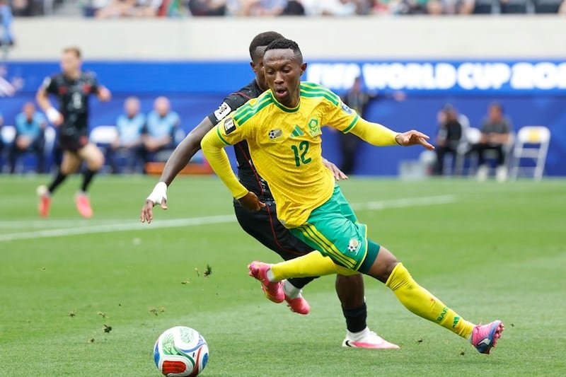Soccer player in a yellow-green kit lunges to kick the ball during a World Cup match, stadium in the background.